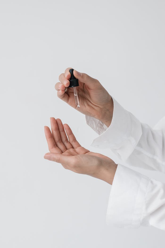 hero-img-02 A person's hands applying skincare serum using a dropper for a beauty routine.